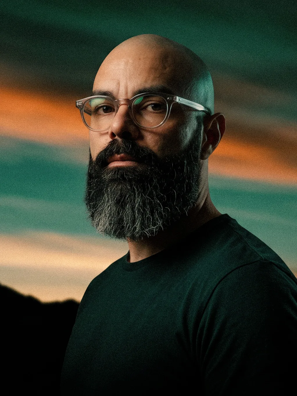 Portrait of Leo Becker, with glasses and a beard, against a sunset sky